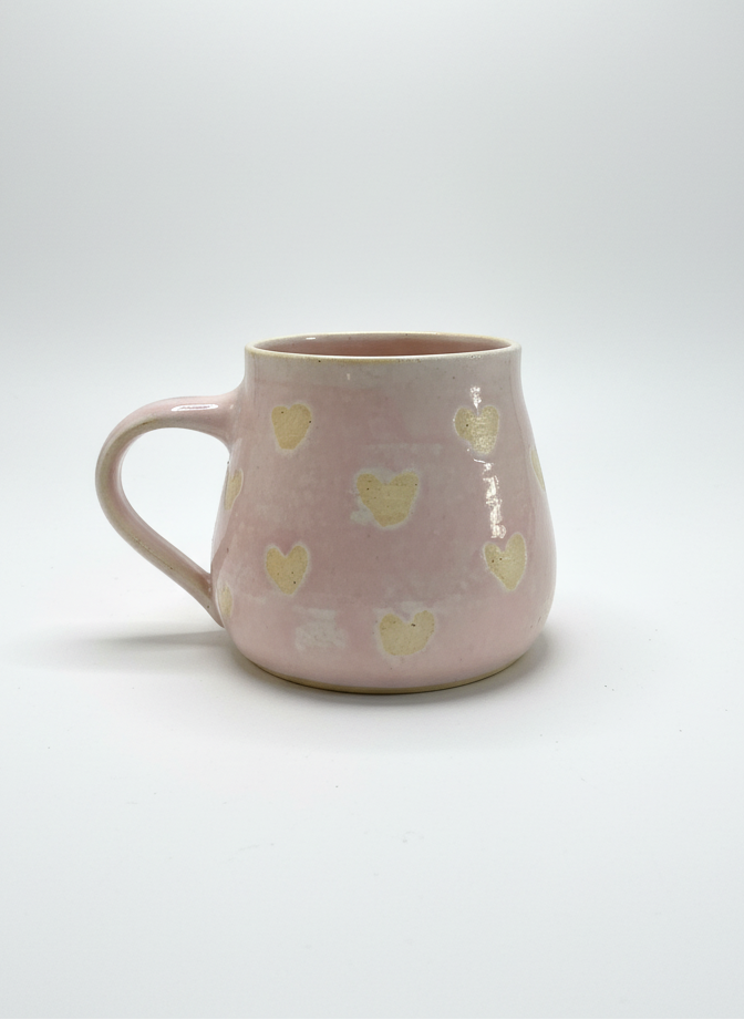 Pink mug with yellow heart patterns on a white background