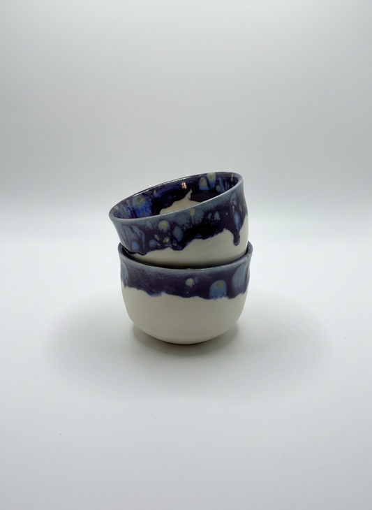 Two ceramic bowls with blue and white glaze stacked on a light gray background